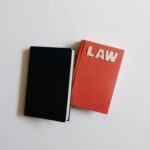 Ilustrasi hukum dengan simbol keadilan (timbangan), gavel, dan buku undang-undang di atas meja kayu.