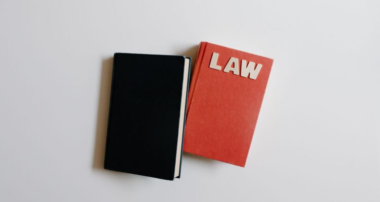 Ilustrasi hukum dengan simbol keadilan (timbangan), gavel, dan buku undang-undang di atas meja kayu.